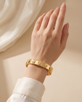 Gentle Shine Bangle worn on the wrist: wide gold-tone bangle with five-petal flowers | Gentle Shine bangle om de pols: brede goudkleurige armband met bloemetjes