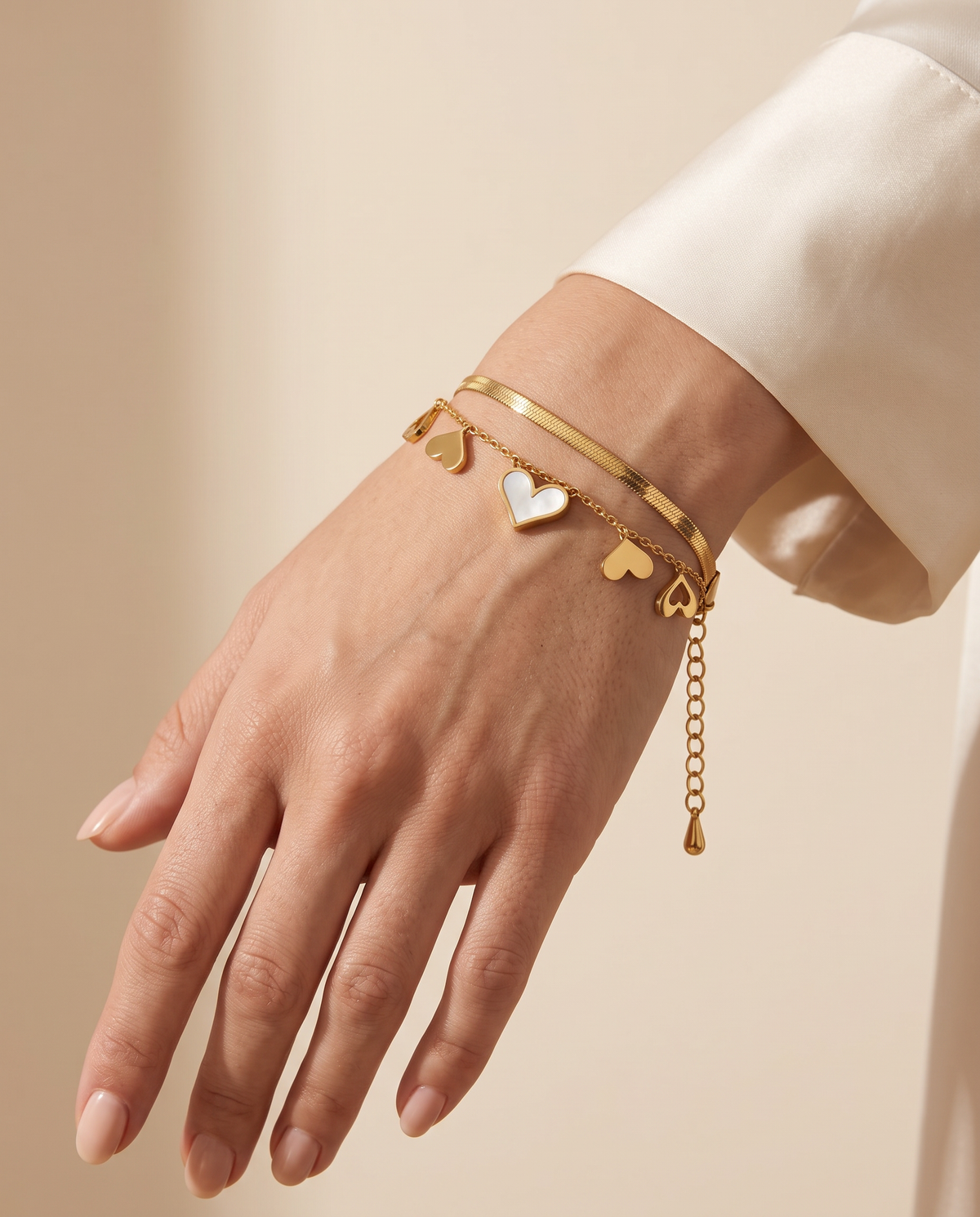Endless Glow Bracelet worn on the wrist: herringbone chain and fine chain with five heart charms | Endless Glow armband om de pols: visgraatketting en fijne ketting met vijf hartjes